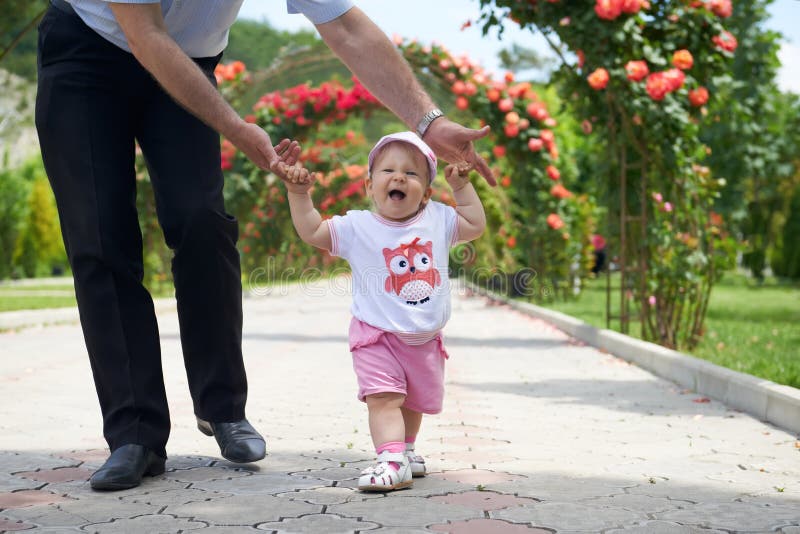 Summer walk. Childs first steps in the fathers strong hands