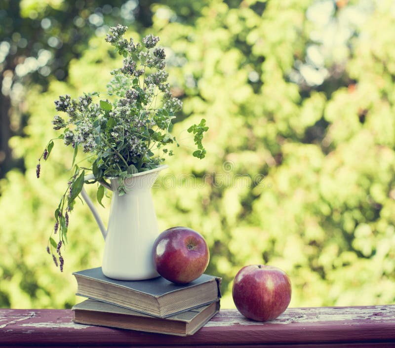 Summer wild flowers in glass vase, old books and apples.
