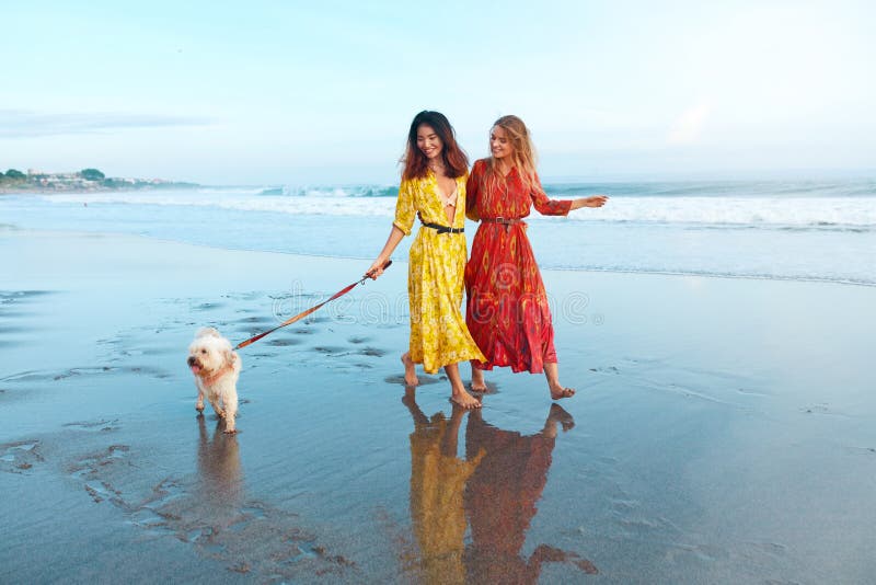 Summer. Women With Dog On Beach. Fashion Girls In Maxi Bohemian Clothing Walking With Pet On Dog-Friendly Coast stock photos