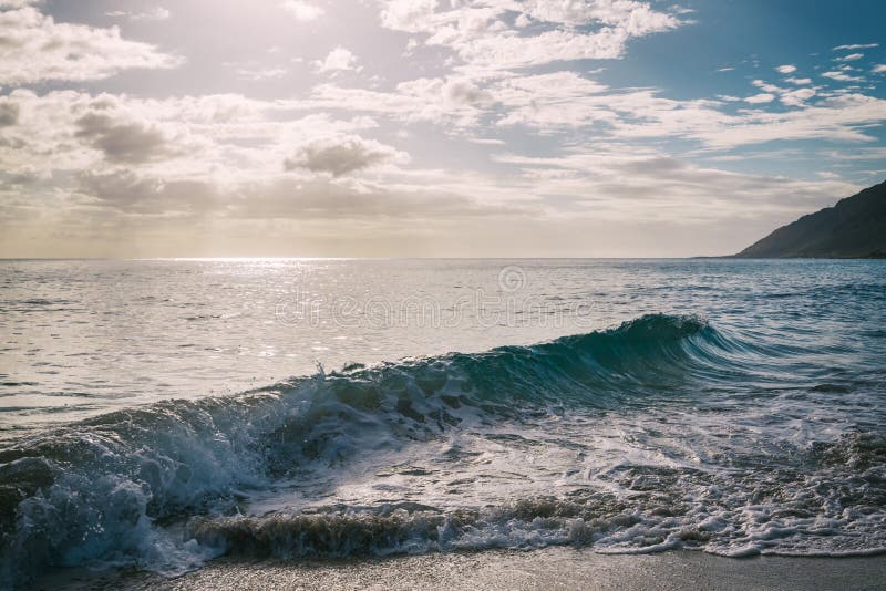 Sun, der durch die Wolken am sandigen Strand mit Wellen scheint lizenzfreie stockbilder Sun, der durch die Wolken am sandigen Strand mit Wellen scheint lizenzfreie stockbilder