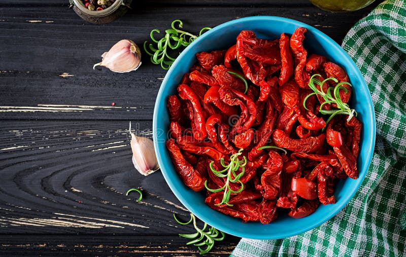 Sun dried tomatoes with herbs and garlic in bowl on wooden table.