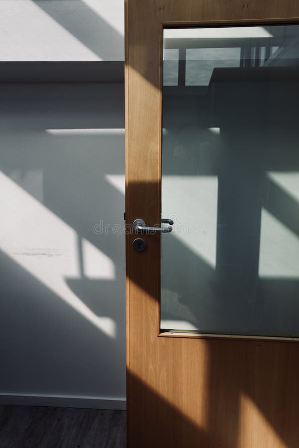 Sun light falling through a window on a wall and door of an office building creating geometrical shadows. Sun light falling through a window on a wall and door of an office building creating geometrical shadows