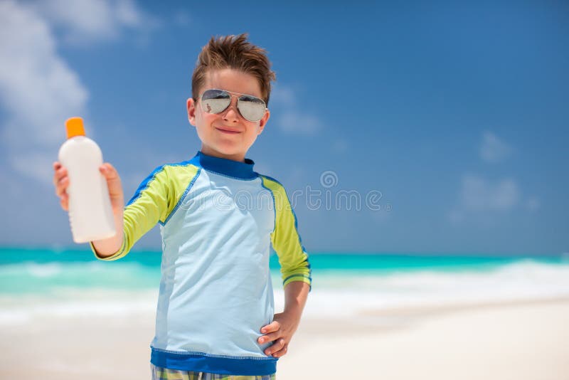 Cute little boy in spiaggia tropicale in possesso di un flacone di crema solare.