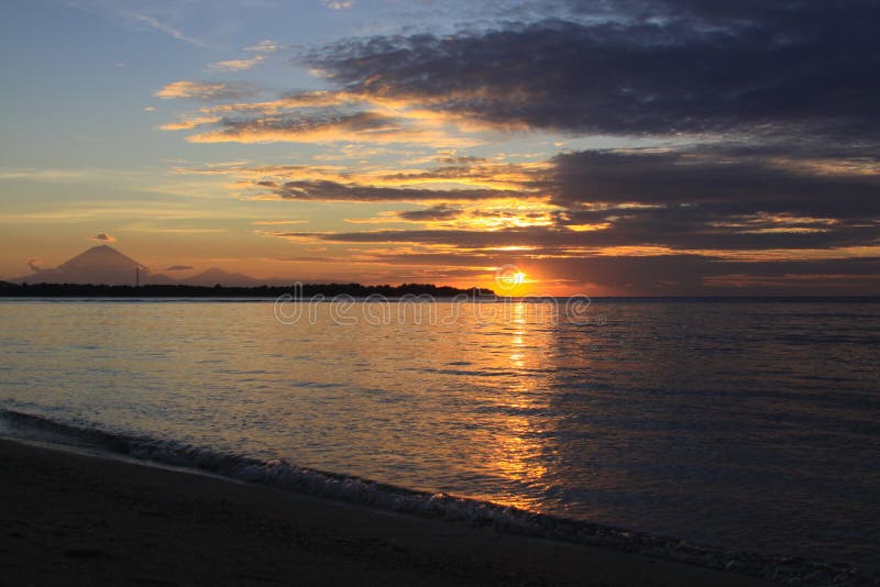 Sun shining from behind clouds with island silhouette