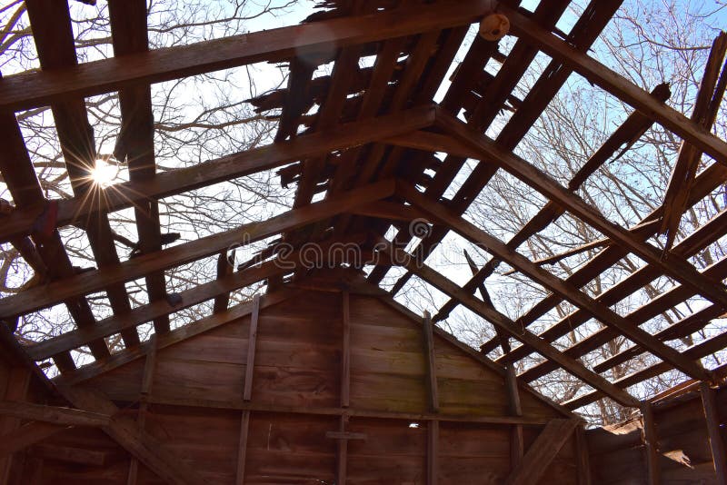 The sun peeks into the open roof of an old barn. Trees and blue skies look down on the old roof and barn wood. The sun peeks into the open roof of an old barn. Trees and blue skies look down on the old roof and barn wood.