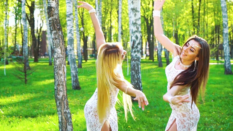 Sun-Strahlen auf den blonden und brunette Frauen in den ähnlichen Kostümen, die in sonnenbeschienen Park tanzen