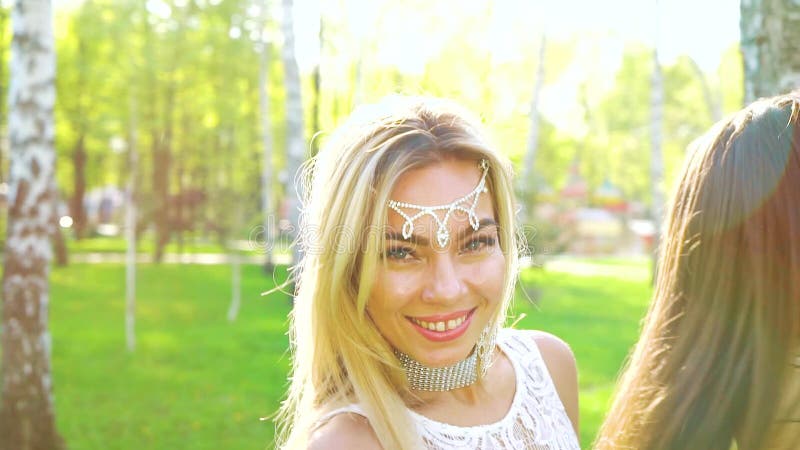 Sun-Strahlen auf den blonden und brunette Frauen in den ähnlichen Kostümen tanzen in sonnenbeschienen Park