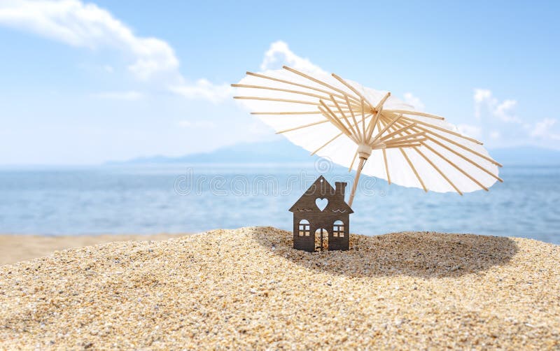 Sun umbrella and house on sandy beach, blue sky and sea in the background. Investment in resort real estate concept