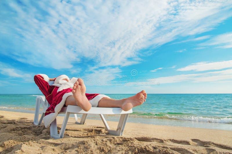 Sunbathing Santa Claus relaxing in bedstone on tropical beach