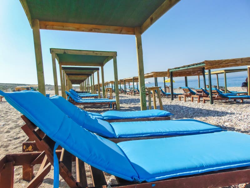 Sunbeds onder stro sunshades op het lege kiezelsteenstrand stock fotografie Sunbeds onder stro sunshades op het lege kiezelsteenstrand stock fotografie