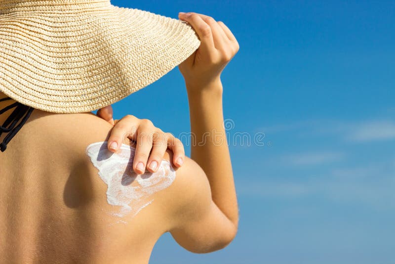 Sunblock de la protección solar Mujer en un sombrero que pone la crema solar en hombro al aire libre bajo sol en día de verano he
