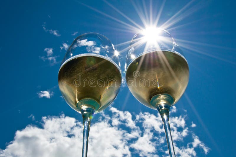 Closeup of two wineglasses with a sun burst filled with white wine side by side with bright blue sky & clouds in the background. Clear closeup view stock images, royalty-free photos and pictures