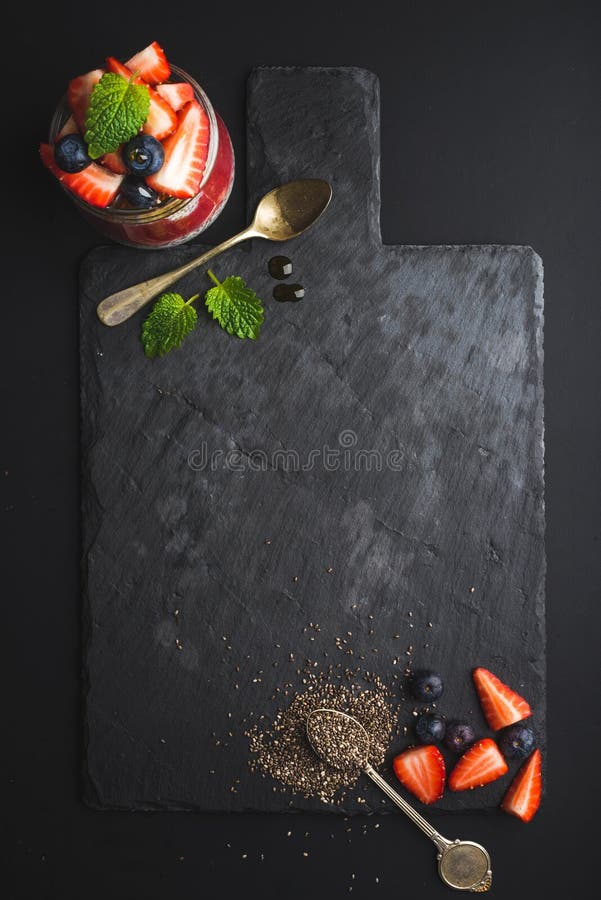 Sund ram för frukostmat Chia pudding med nya bär och mintkaramellen på svart kritiserar stenbrädet över mörk bakgrund royaltyfria bilder Sund ram för frukostmat Chia pudding med nya bär och mintkaramellen på svart kritiserar stenbrädet över mörk bakgrund royaltyfria bilder