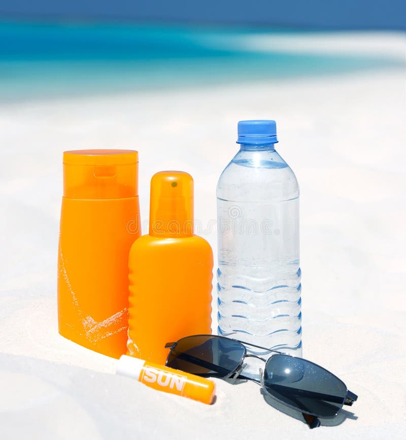 Occhiali da sole, acqua e crema di protezione solare in spiaggia sfondo.
