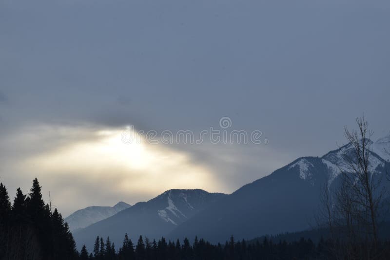 Sunlight Being Blocked By Clouds Over Snowy Mountain Peaks Stock Photo