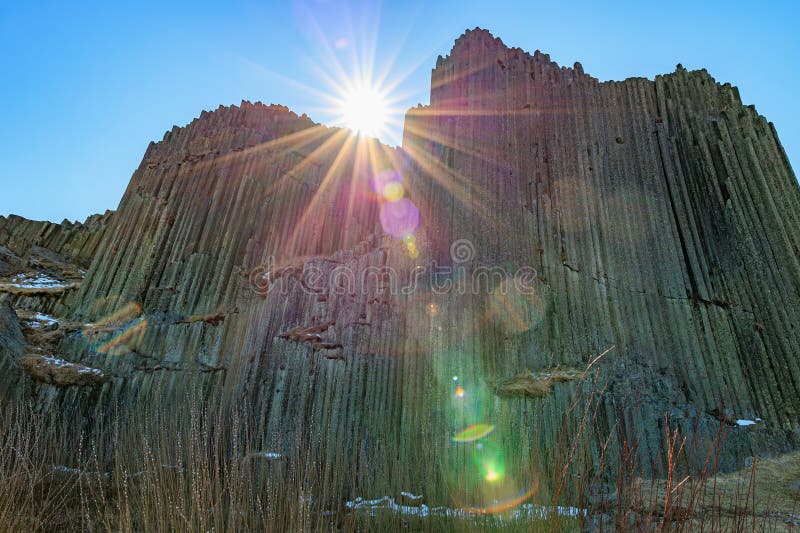 Sunlit basalt cliffs with lens flare and clear sky royalty free stock photo