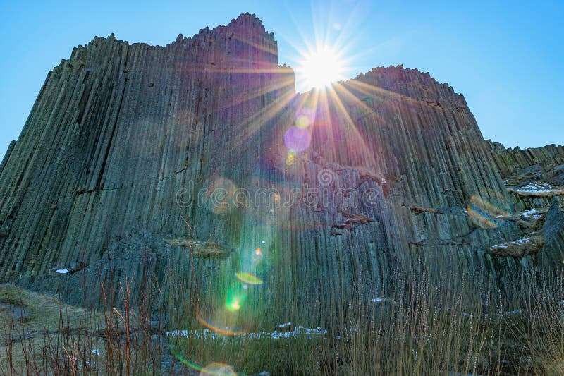 Sunlit geometric basalt columns with lens flare and clear blue sky stock photography