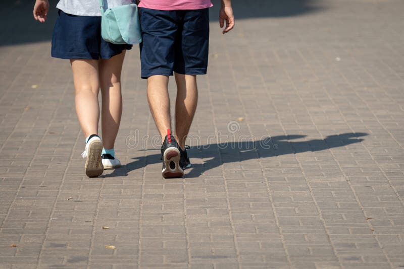 On a sunny day, a couple of people walk along the sidewalk. The human shadows are visible on the sidewalk. View from the back. stock photography On a sunny day, a couple of people walk along the sidewalk. The human shadows are visible on the sidewalk. View from the back. stock photography