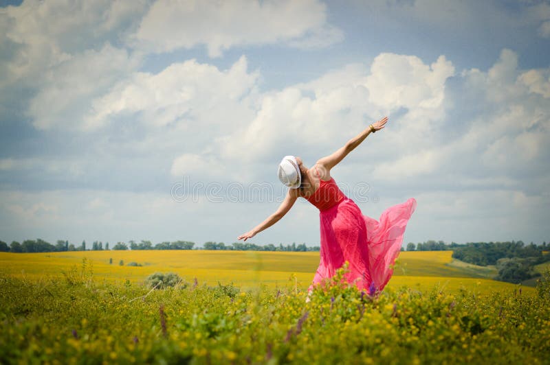 Sunny freedom: image of beautiful blond young woman in pink dress having fun dancing on green summer outdoors blue sky copy space