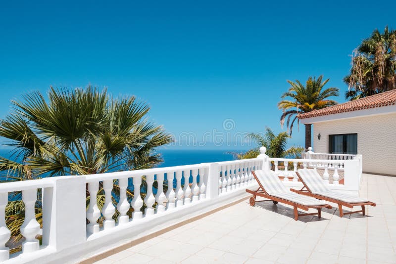 Sunny terrace with sun beds of ocean view house with palm trees anb blue sky copy space