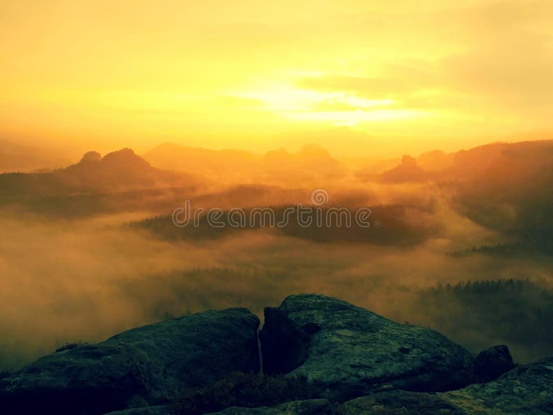 Sunrise in a beautiful mountain of Czech-Saxony Switzerland. Hilly peaks increased from orange fog with sun rays.