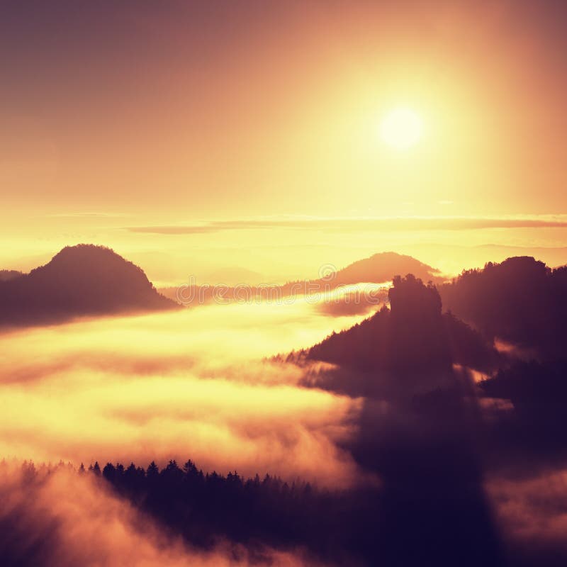 Sunrise in a beautiful mountain of Czech-Saxony Switzerland. Sandstone peaks increased from fog, the fog is orange due to sun rays