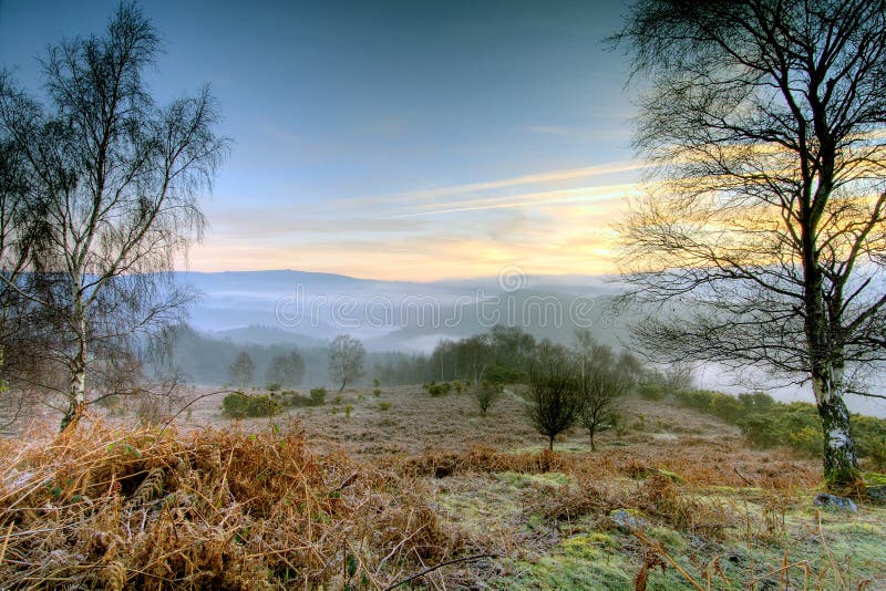 Sunrise near Leigh Tor on Dartmoor with pastel morning light and mist filling the valley beyond. Sunrise near Leigh Tor on Dartmoor with pastel morning light and mist filling the valley beyond