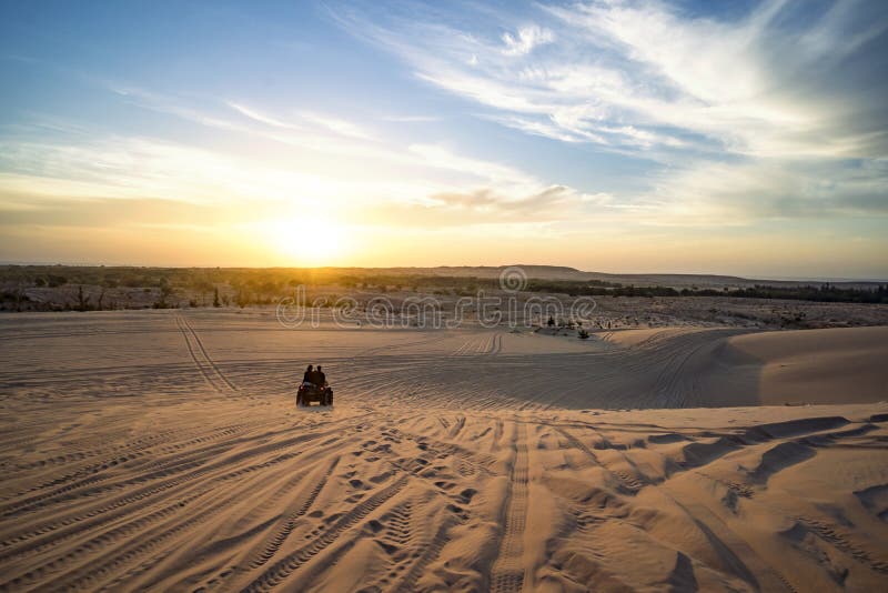 Sunrise in desert. Scene with two ATV bikers. Tourists ride on an off-road ATV through the sand dunes of the Vietnamese