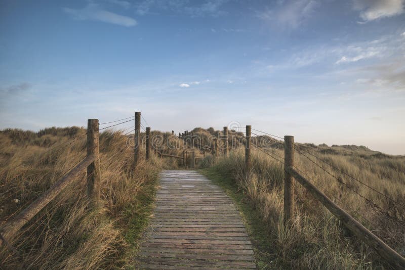 Beautiful sunrise landscape image of sand dunes system over beach with wooden boardwalk