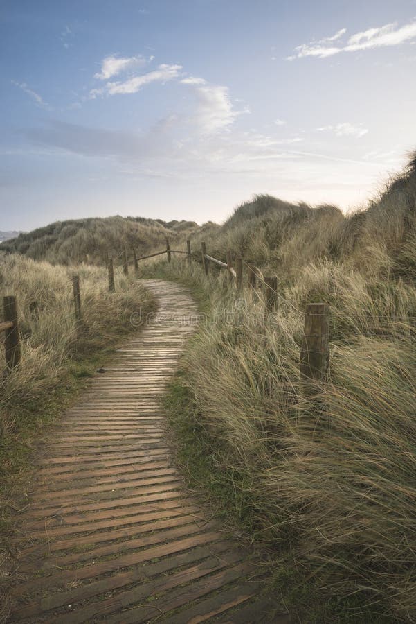 Beautiful sunrise landscape image of sand dunes system over beach with wooden boardwalk