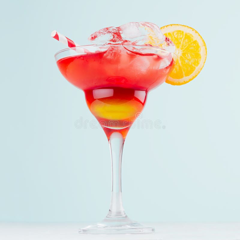 Sunrise layered red, yellow drinks with orange, straw, ice cubes in elegant glass on pastel blue background, white wood table.