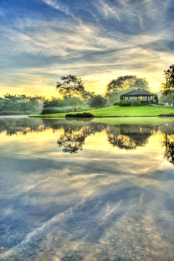 HDR trattamento di alba poco dopo l'alba sulle rive di un lago ancora con un padiglione sulla sua banca.