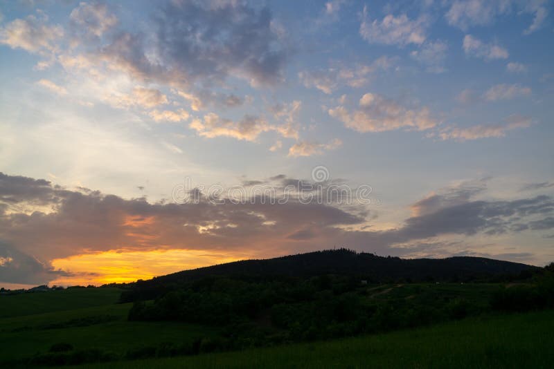 Východ alebo západ slnka nad kopcami a lúkou.