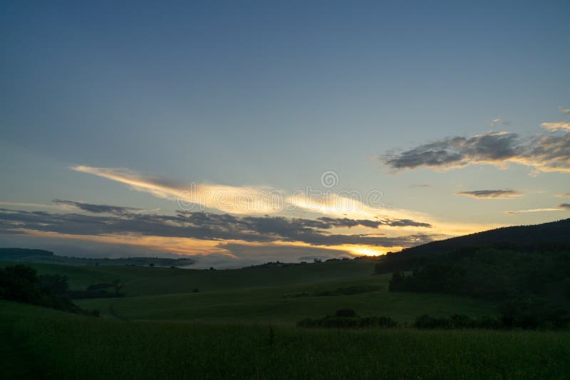 Východ alebo západ slnka nad kopcami a lúkou.