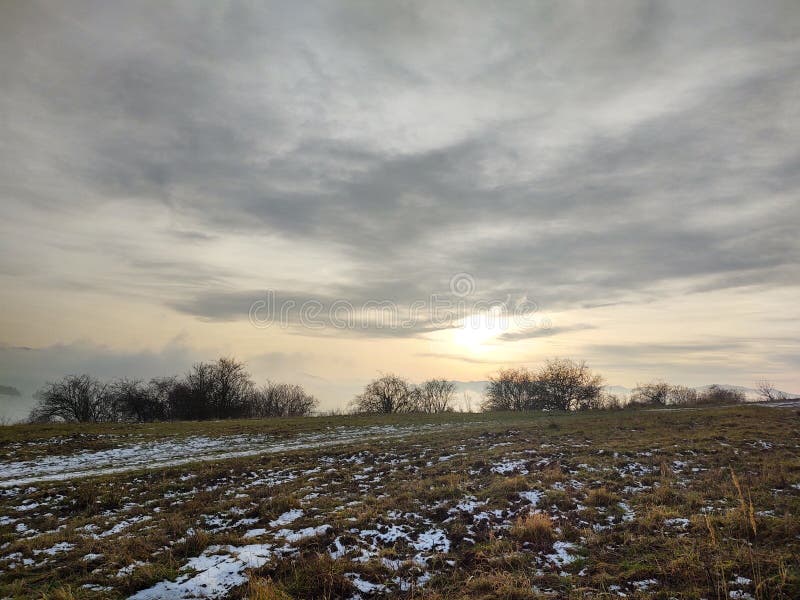 Východ nebo západ slunce nad kopci a loukou.