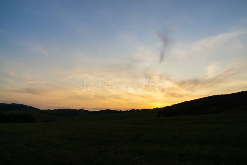 Východ nebo západ slunce nad kopci a loukou.