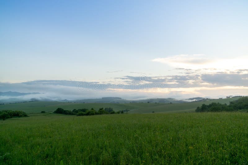 Východ alebo západ slnka nad kopcami a lúkou.