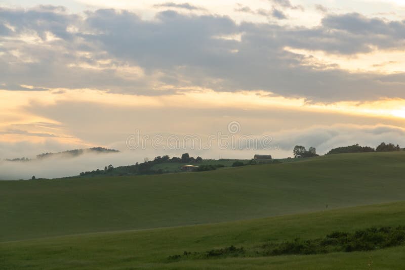 Východ nebo západ slunce nad kopci a loukou.