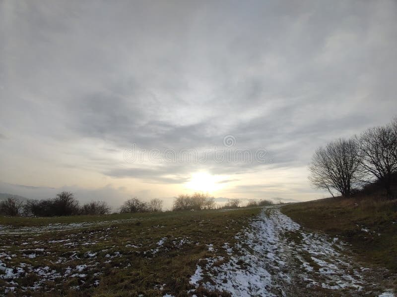 Východ nebo západ slunce nad kopci a loukou.