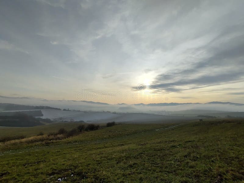 Východ nebo západ slunce nad kopci a loukou.