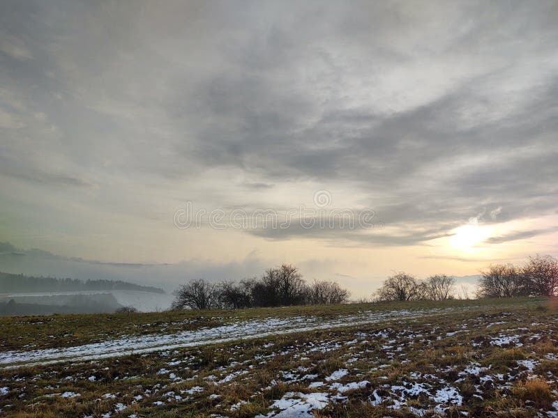 Východ nebo západ slunce nad kopci a loukou.