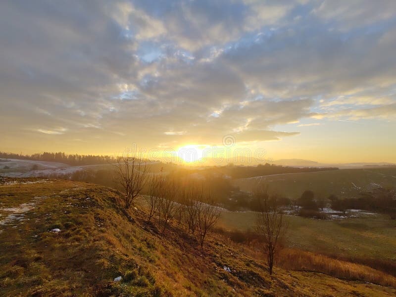 Východ nebo západ slunce nad kopci a loukou.