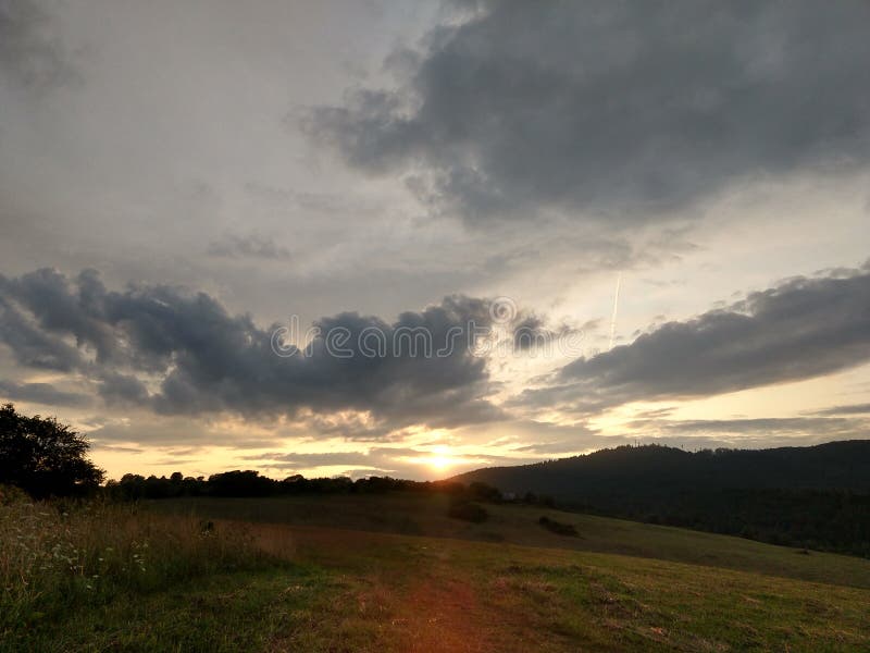 Východ nebo západ slunce nad kopci a loukou.