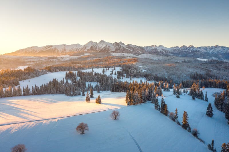 Sunrise in winter mountains. Scenic nature of snowy summits of mountain range illuminated by sun. Aerial view of mountains in