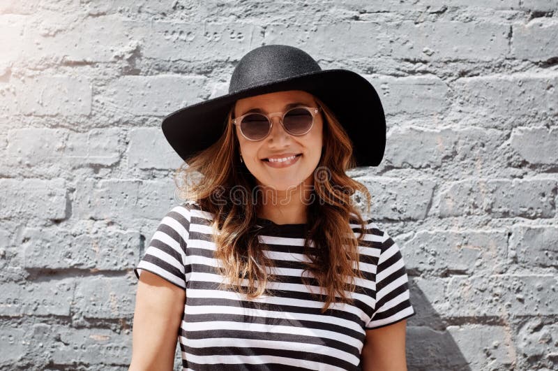 Suns out, let the good times roll. Portrait of an attractive young woman posing against a brick wall outdoors.