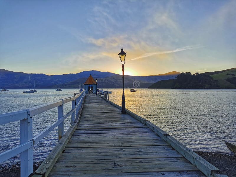 Sunset at Akaroa harbour pier with an old street light. New Zealand.