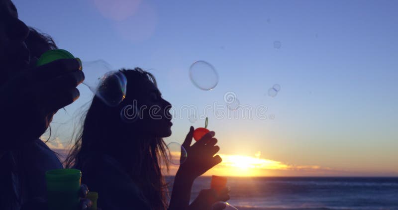 Sunset, beach bubbles and silhouette of friends on outdoor bonding time, have fun and relax on ocean sea shore. Blue sky