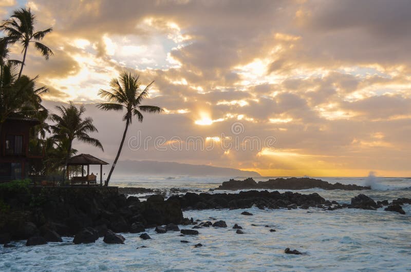 Sunset breaking through the clouds as waves splash in on the rocks in Hawaii