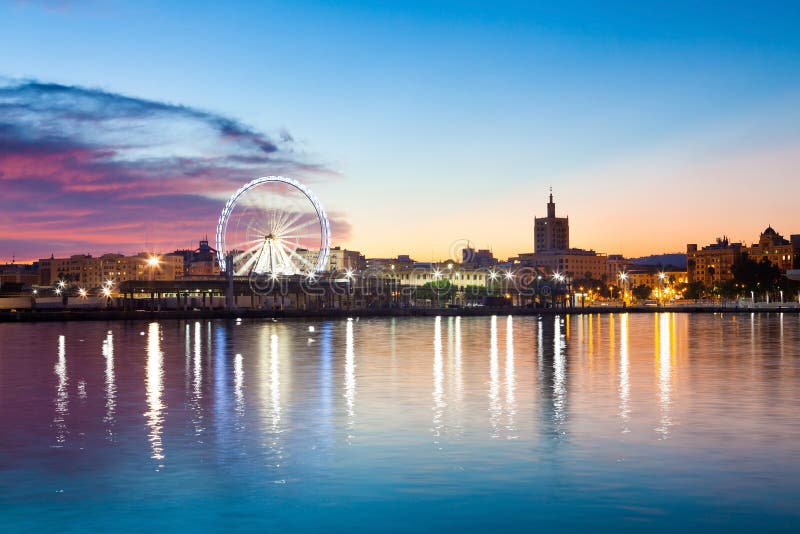 Sunset cityscape with ferris wheel in motion. Malaga city, Spain