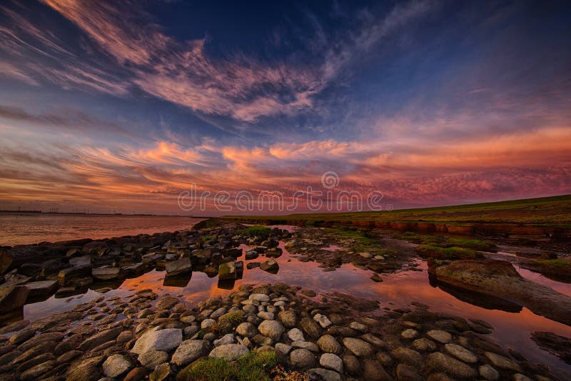 The sun sets on the Dollard in Groningen, the Netherlands filling the sky with burning colours. The Dollard is a bay in the Wadden mud flats sea. The sun sets on the Dollard in Groningen, the Netherlands filling the sky with burning colours. The Dollard is a bay in the Wadden mud flats sea.